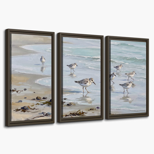 Small shorebirds standing along a pale blue shoreline 3 piece framed canvas wall art on a white background