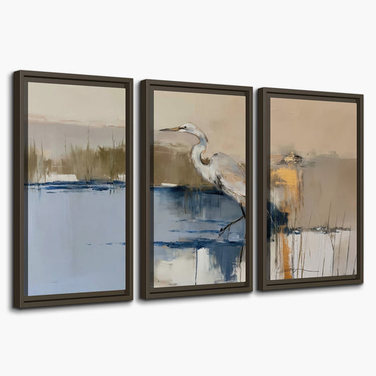 A slender heron standing in blue water among loose ochre and cream brushstrokes 3 piece framed canvas wall art on a white background
