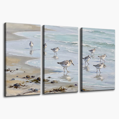 Small shorebirds standing along a pale blue shoreline 3 piece canvas wall art on a white background