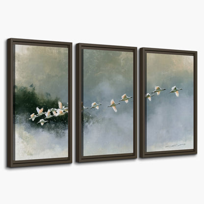 A flock of white birds flying low above a quiet blue-green lake 3 piece framed canvas wall art on a white background