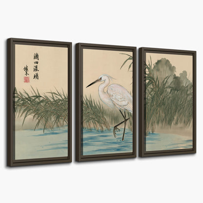 A white heron standing beside a quiet river with reeds and distant hills 3 piece framed canvas wall art on a white background