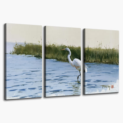 A white heron wading through bright blue water beside green reeds 3 piece canvas wall art on a white background