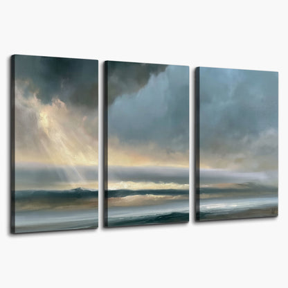 Dramatic blue-gray storm clouds breaking over a pale strip of ocean light 3 piece canvas wall art on a white background