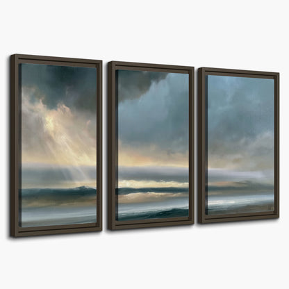 Dramatic blue-gray storm clouds breaking over a pale strip of ocean light 3 piece framed canvas wall art on a white background