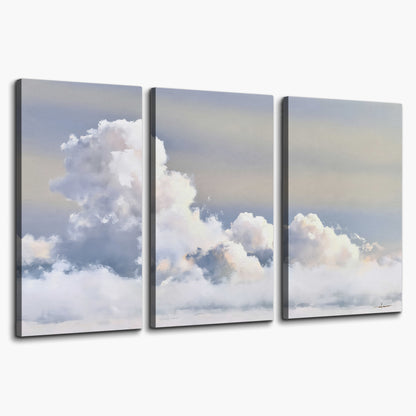 Large white clouds rising through a pale blue sky with gentle warm highlights 3 piece canvas wall art on a white background