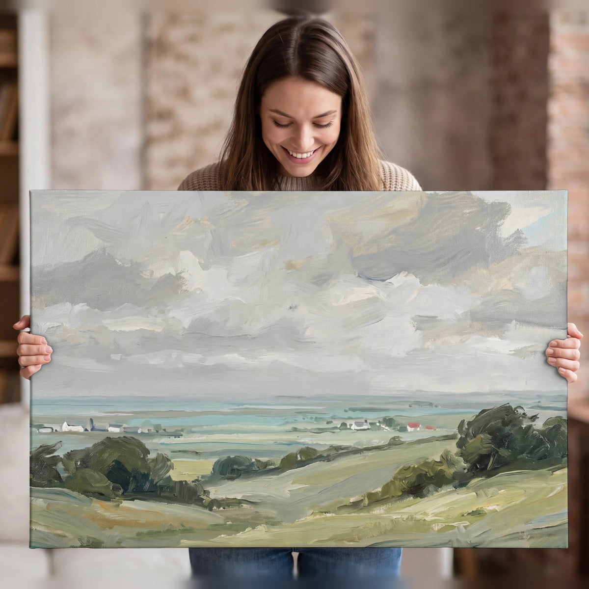 Woman holding a stretched canvas print of a coastal countryside oil painting with seaside village