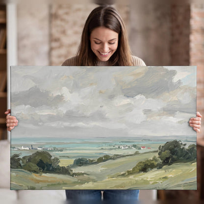 Woman holding a stretched canvas print of a coastal countryside oil painting with seaside village