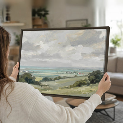 Woman holding a framed canvas of a coastal countryside oil painting in her living room