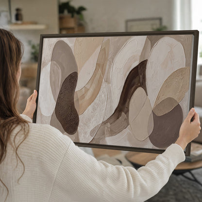 Layered organic shapes in taupe, cream and brown single framed canvas wall art held in hands