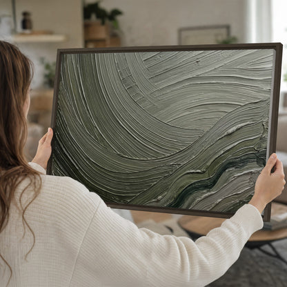 Olive and sage green abstract flowing waves with curved painted-style ridges single framed canvas wall art held in hands