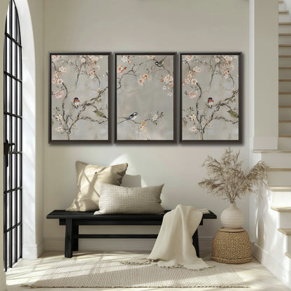 Small songbirds among pink and cream blossoms, green leaves and delicate branches on gray 3 piece framed canvas wall art displayed in a entryway