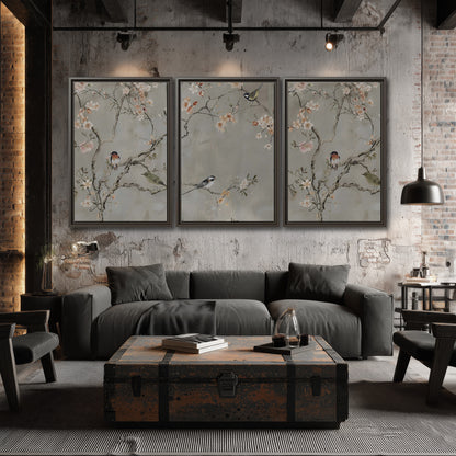 Small songbirds among pink and cream blossoms, green leaves and delicate branches on gray 3 piece framed canvas wall art displayed in a industrial room