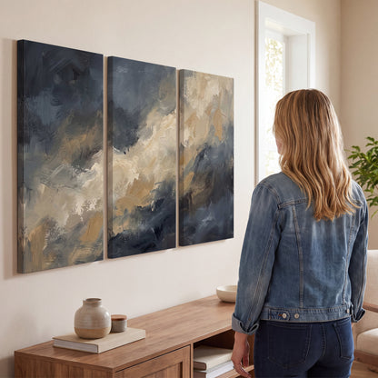 Sweeping charcoal and cream painted clouds with warm gold tones 3 piece canvas wall art three panel arrangement on a wall