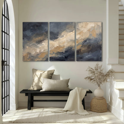 Sweeping charcoal and cream painted clouds with warm gold tones 3 piece canvas wall art displayed in a entryway