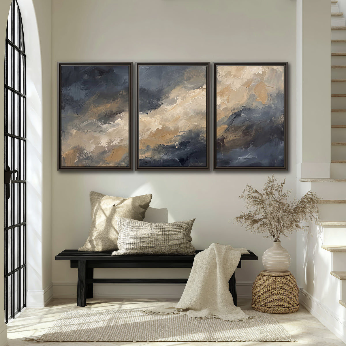 Sweeping charcoal and cream painted clouds with warm gold tones 3 piece framed canvas wall art displayed in a entryway