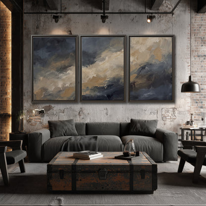 Sweeping charcoal and cream painted clouds with warm gold tones 3 piece framed canvas wall art displayed in a industrial room