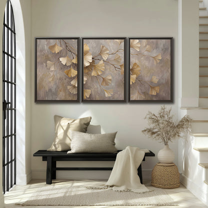 Cream and gold-colored ginkgo leaves against warm gray 3 piece framed canvas wall art displayed in a entryway