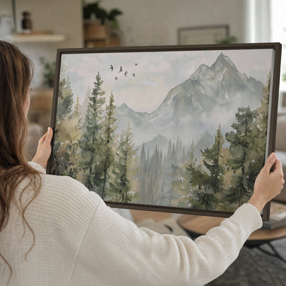 Soft green mountain peaks and evergreen trees beneath birds single framed canvas wall art held in hands