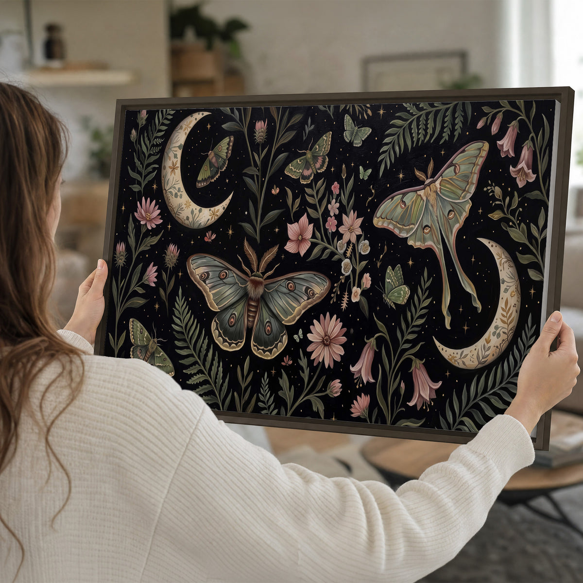 Decorative moths, crescent moons and flowers on black single framed canvas wall art held in hands