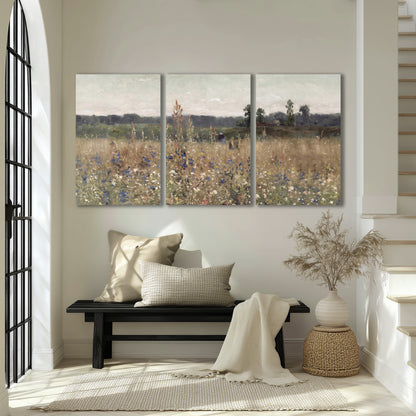 A loose painterly meadow with scattered blue and white wildflowers 3 piece canvas wall art displayed in a entryway