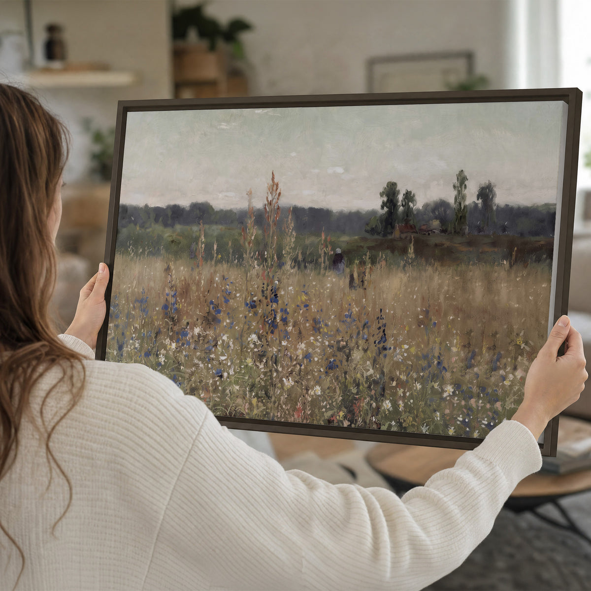 A loose painterly meadow with scattered blue and white wildflowers single framed canvas wall art held in hands