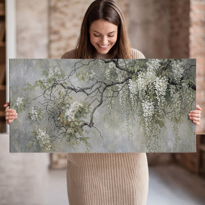 Trailing white blossoms and delicate green branches on pale gray single canvas wall art held in hands