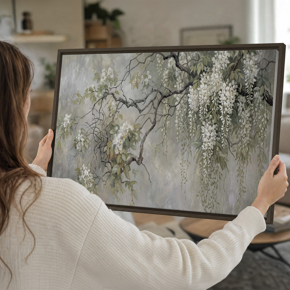 Trailing white blossoms and delicate green branches on pale gray single framed canvas wall art held in hands