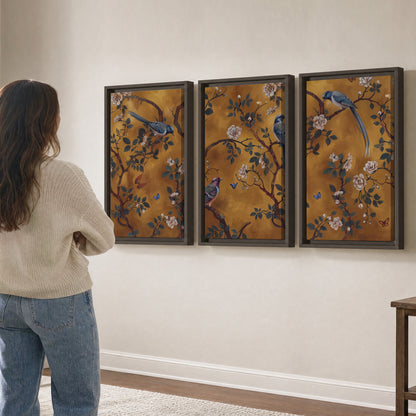 Colorful perched birds and pale blossoms on an ochre background 3 piece framed canvas wall art three panel arrangement on a wall