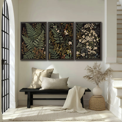 Layered green ferns and delicate cream flowers on a black background 3 piece framed canvas wall art displayed in a entryway