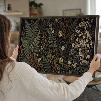 Layered green ferns and delicate cream flowers on a black background single framed canvas wall art held in hands