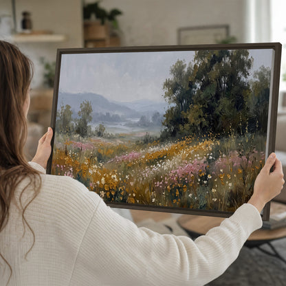 A flower-filled meadow overlooking soft blue mountain ridges single framed canvas wall art held in hands