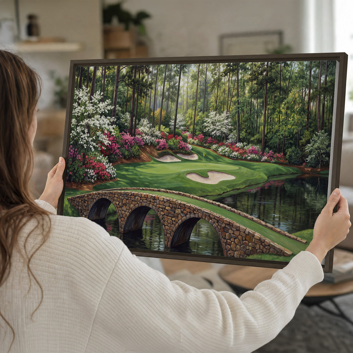 An arched stone bridge beside a landscaped golf course and reflective pond single framed canvas wall art held in hands