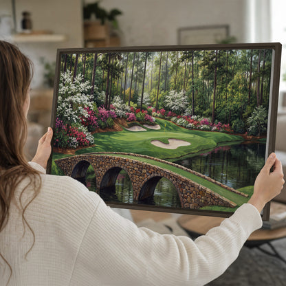 An arched stone bridge beside a landscaped golf course and reflective pond single framed canvas wall art held in hands
