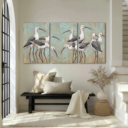 Long-legged white and gray wading birds against a muted aqua background 3 piece canvas wall art displayed in a entryway