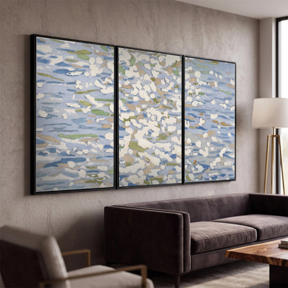 Loose pale blue, white and soft green marks suggesting shimmering water 3 piece framed canvas wall art displayed in a modern living room