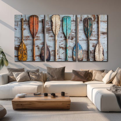 A row of colorful weathered wooden oars against pale blue boards 3 piece canvas wall art displayed in a living room