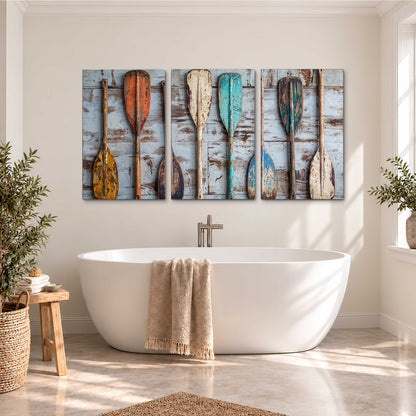 A row of colorful weathered wooden oars against pale blue boards 3 piece canvas wall art styled in an interior