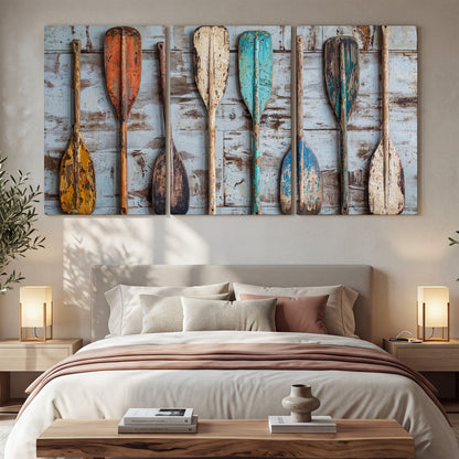 A row of colorful weathered wooden oars against pale blue boards 3 piece canvas wall art displayed in a bedroom