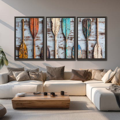 A row of colorful weathered wooden oars against pale blue boards 3 piece framed canvas wall art displayed in a living room