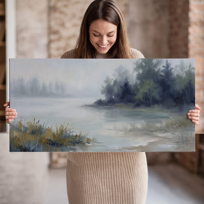 A calm pale lake bordered by dark evergreen trees and distant mist single canvas wall art held in hands