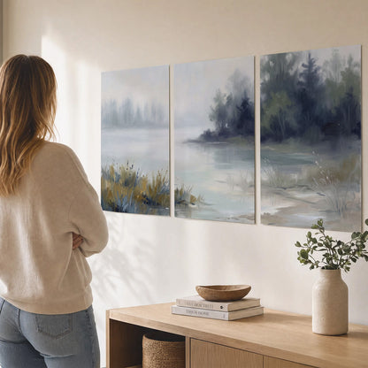 A calm pale lake bordered by dark evergreen trees and distant mist set of 3 poster prints three panel arrangement on a wall