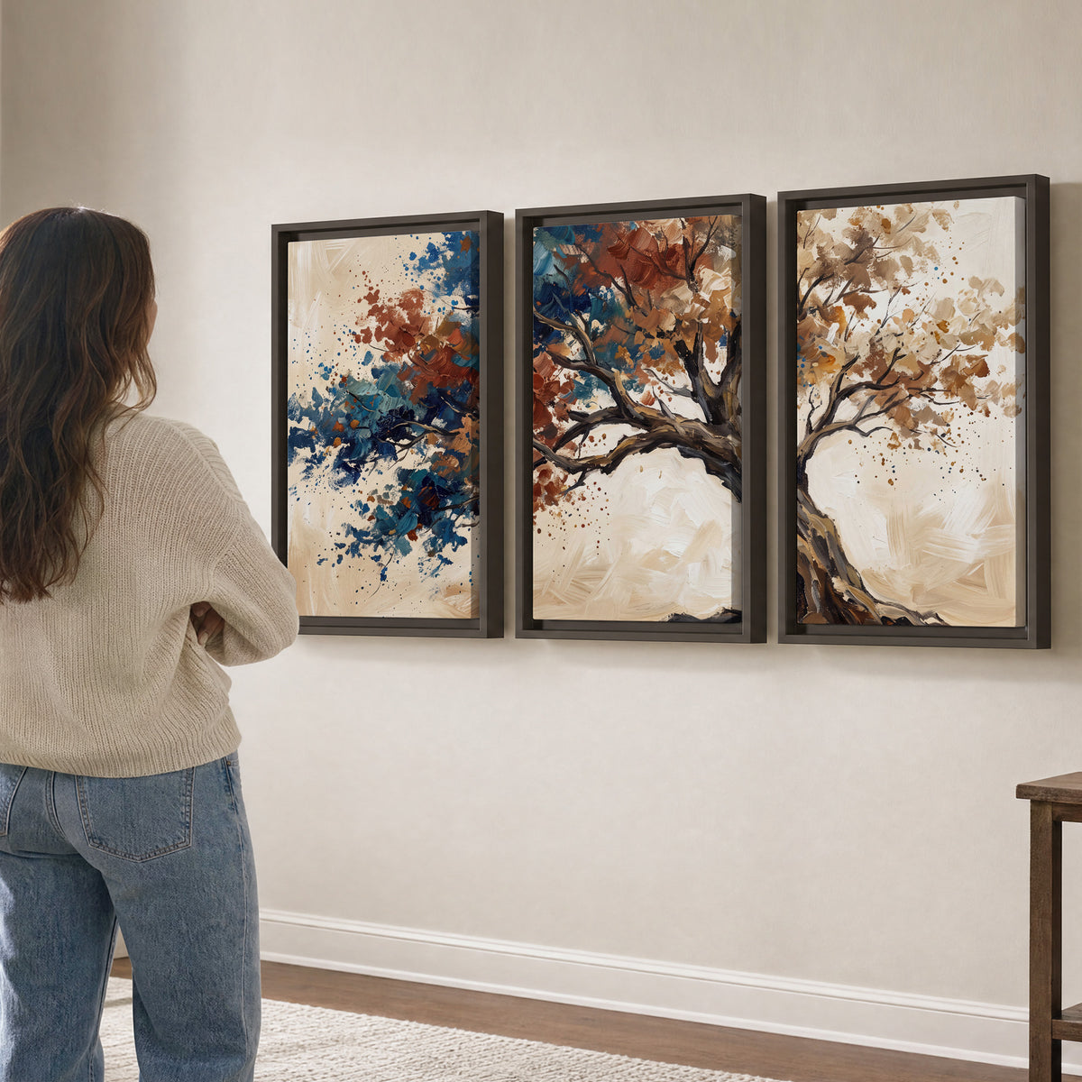 A broad tree with rust, blue and ochre foliage against warm cream 3 piece framed canvas wall art three panel arrangement on a wall