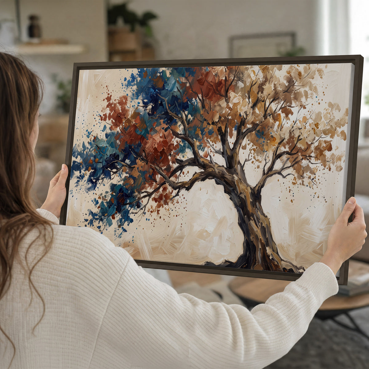 A broad tree with rust, blue and ochre foliage against warm cream single framed canvas wall art held in hands