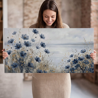 Soft blue flowers and ivory grasses beside a pale coastal horizon single canvas wall art held in hands