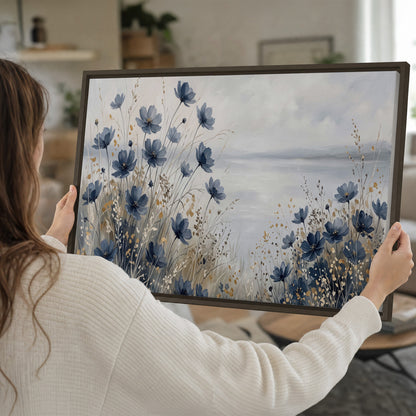 Soft blue flowers and ivory grasses beside a pale coastal horizon single framed canvas wall art held in hands