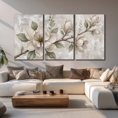 Large ivory magnolia blossoms and soft green leaves on pale gray 3 piece canvas wall art displayed in a living room