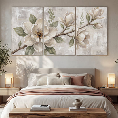 Large ivory magnolia blossoms and soft green leaves on pale gray 3 piece canvas wall art displayed in a bedroom