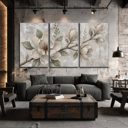 Large ivory magnolia blossoms and soft green leaves on pale gray 3 piece canvas wall art displayed in a industrial room