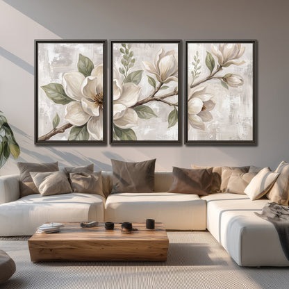 Large ivory magnolia blossoms and soft green leaves on pale gray 3 piece framed canvas wall art displayed in a living room