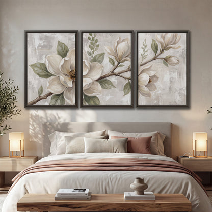 Large ivory magnolia blossoms and soft green leaves on pale gray 3 piece framed canvas wall art displayed in a bedroom